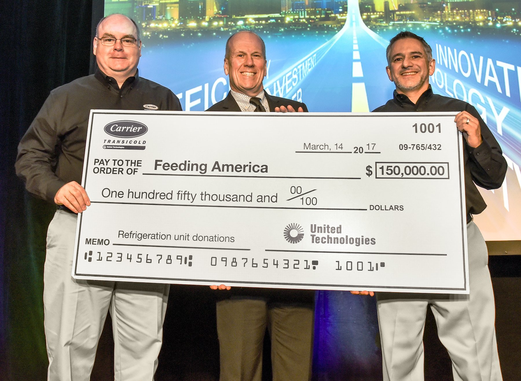 Tom Ondo left vice president amp general manager Americas TruckTrailerRail and Jon Shaw right director Global Communications amp Sustainability Carrier Transicold amp Refrigeration Systems present a 150000 check to Bill Thomas chief supply chain officer Feeding America for the donation and installation of transport refrigeration units to seven Feeding America member food banks across the US