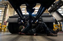 A fleet technician works under a truck chassis.