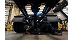 A fleet technician works under a truck chassis.