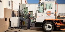 A driver charges an Orange EV battery-electric terminal tractor.