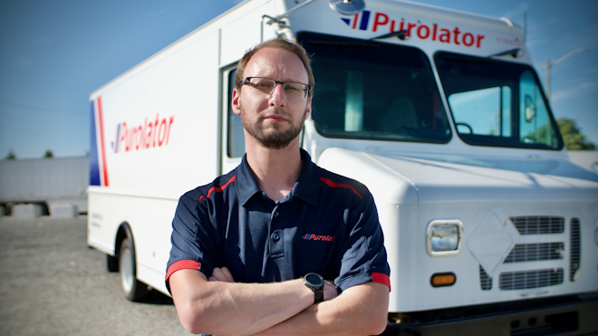 A Purolator driver is shown in front of a Motive EPIC Class 6 step van.