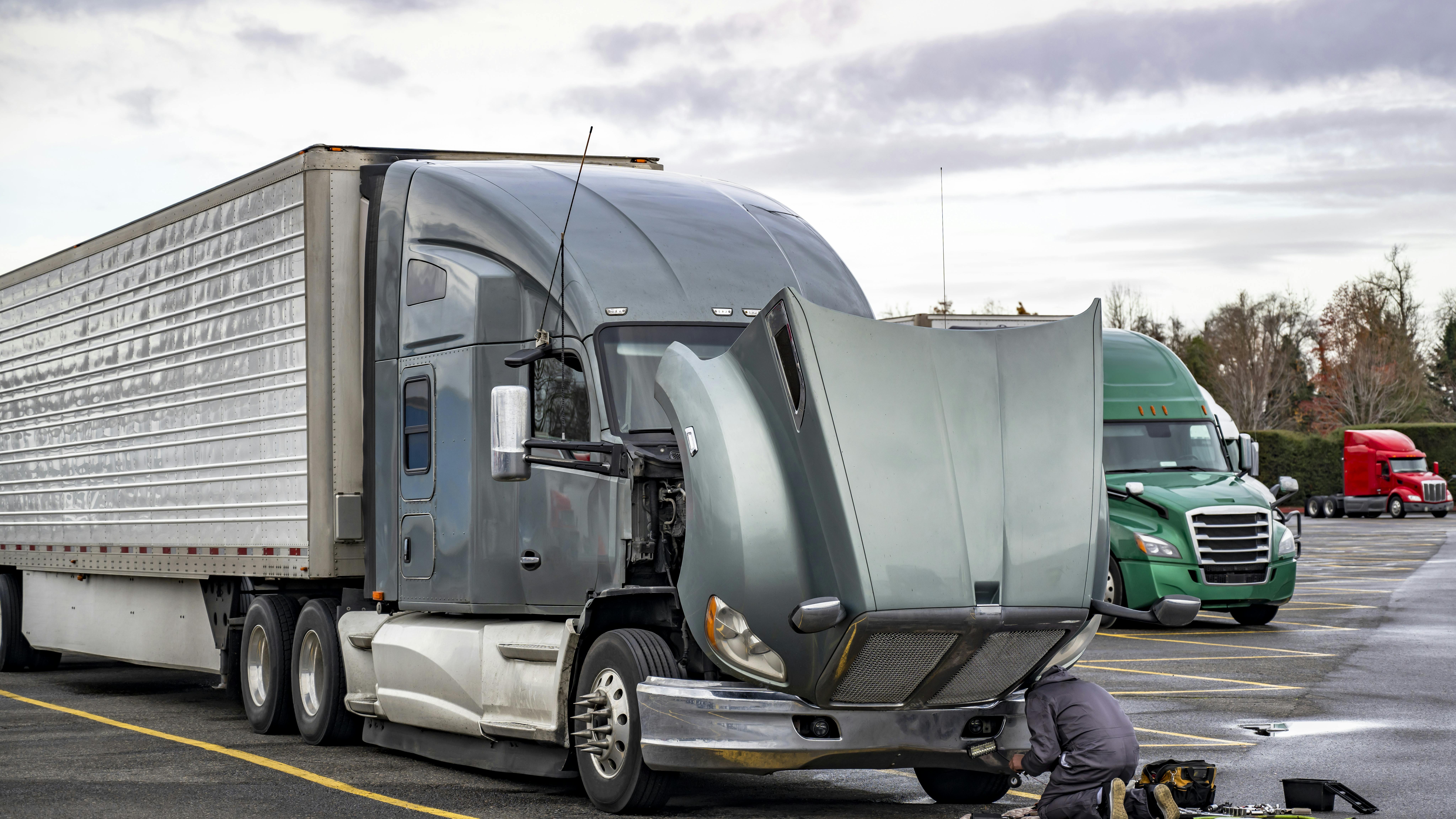 truck driver repairs a semi truck at a rest area
