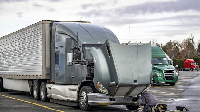 truck driver repairs a semi truck at a rest area