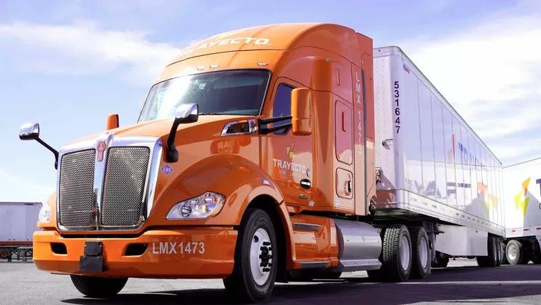 An orange Kenworth Mexicana truck in a parking lot with the sun shining down