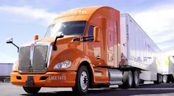 An orange Kenworth Mexicana truck in a parking lot with the sun shining down