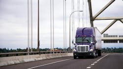Purple semi-truck with a trailer crossing a highway bridge on a cloudy day, representing freight transportation and the trucking industry. Purple semi-truck with a trailer crossing a highway bridge on a cloudy day, representing freight transportation and the trucking industry.