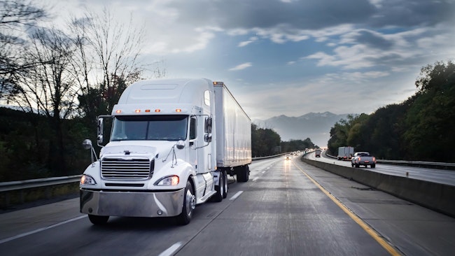 White semi-truck driving on a highway at night, hauling freight with motion blur capturing its speed.