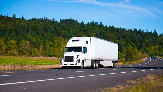 A white semi-truck with a long trailer driving on a winding highway through a picturesque landscape of green hills and trees, emphasizing the blend of nature and modern logistics.
