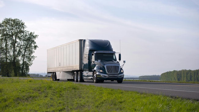 Modern black semi-truck with aerodynamic dry van trailer, highlighting its sleek design and fuel-efficient features on a scenic highway.