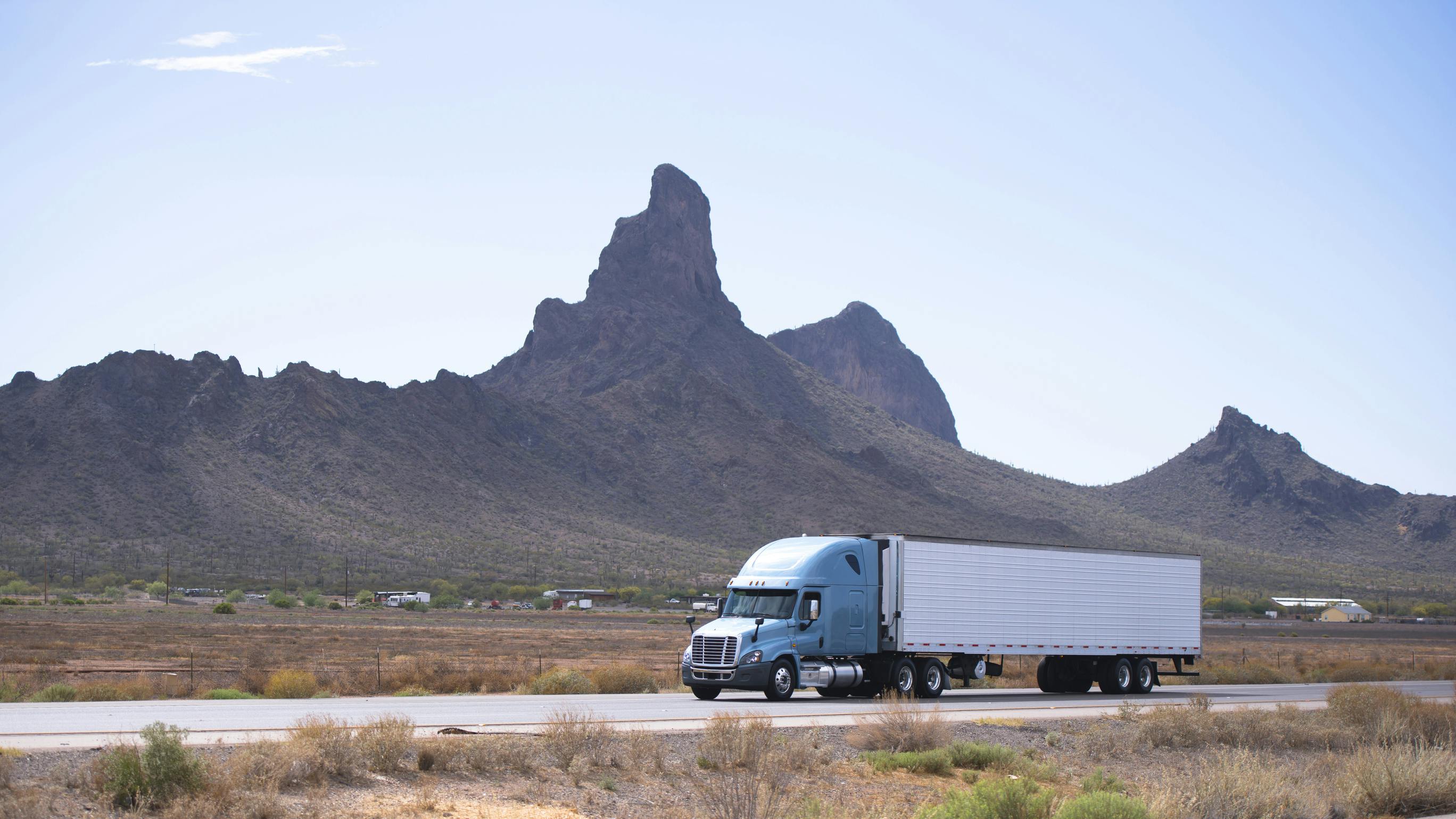 White semi-truck with reefer trailer driving on Arizona highway with mountain backdrop, symbolizing freight transport and long-haul trucking.