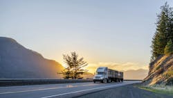 White big rig semi truck transporting boxes of apples on a flatbed trailer during evening on a U.S. highway for long-haul freight delivery White big rig semi truck transporting boxes of apples on a flatbed trailer during evening on a U.S. highway for long-haul freight delivery
