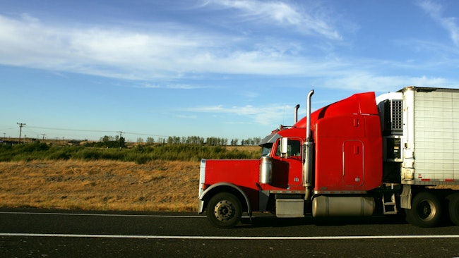 Red semi-truck cab with white trailer driving on a highway, representing long-haul freight and trucking operations