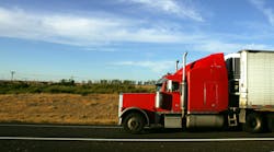 Red semi-truck cab with white trailer driving on a highway, representing long-haul freight and trucking operations Red semi-truck cab with white trailer driving on a highway, representing long-haul freight and trucking operations