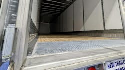 A view looking into the empty cargo space of a new commercial dry van trailer from the open rear doors, featuring a wooden floor, metal interior walls, and a diamond plate threshold. A view looking into the empty cargo space of a new commercial dry van trailer from the open rear doors, featuring a wooden floor, metal interior walls, and a diamond plate threshold.