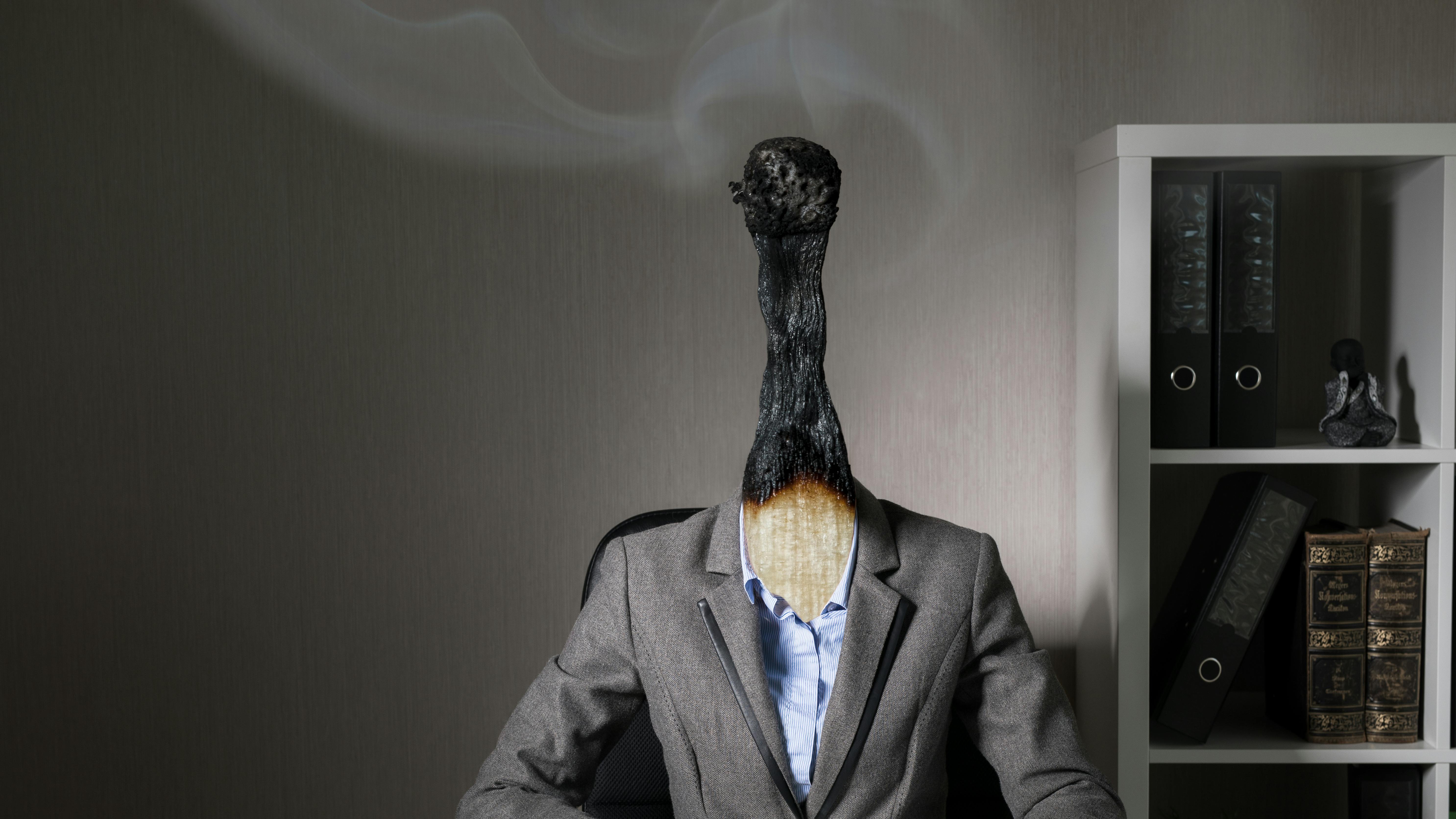 lose-up of a worker with the head of match that is burned out but still smoking, representing modern worker burnout