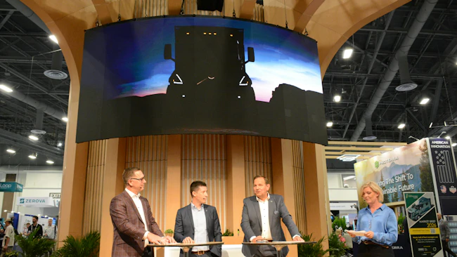 our Volvo executives standing on a stage at ACT Expo beneath a large digital screen displaying the yellow silhouette of a new heavy-duty vocational truck.