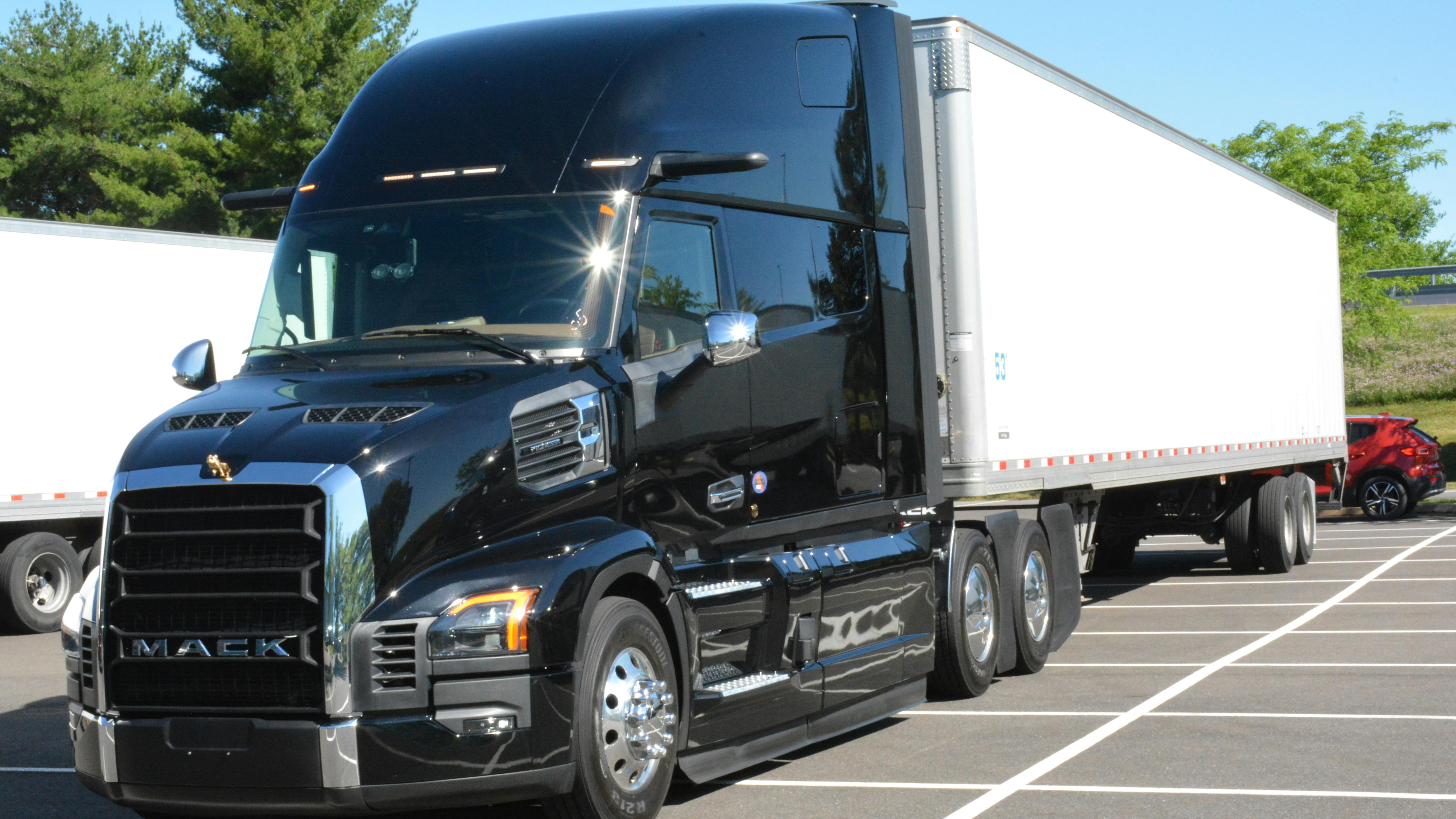 Three-quarter front view of a shiny black Mack Pioneer long-haul tractor hooked to a white 53-foot dry van trailer, parked on a paved lot.