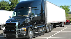 Three-quarter front view of a shiny black Mack Pioneer long-haul tractor hooked to a white 53-foot dry van trailer, parked on a paved lot.