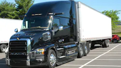 Three-quarter front view of a shiny black Mack Pioneer long-haul tractor hooked to a white 53-foot dry van trailer, parked on a paved lot. Three-quarter front view of a shiny black Mack Pioneer long-haul tractor hooked to a white 53-foot dry van trailer, parked on a paved lot.