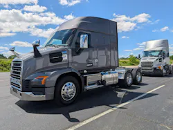 A dark grey Mack Anthem day cab tractor leads a silver day cab on the paved test track at the Mack Experience Center, under a bright, cloudy sky. A dark grey Mack Anthem day cab tractor leads a silver day cab on the paved test track at the Mack Experience Center, under a bright, cloudy sky.