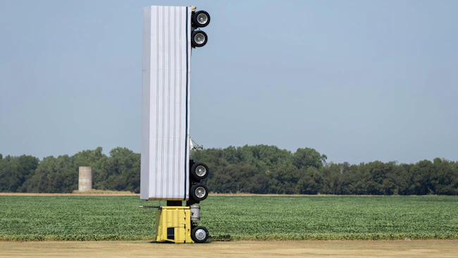 Surreal photo of a commercial semi-truck perched atop a utility pole in an open field, symbolizing a capacity illusio