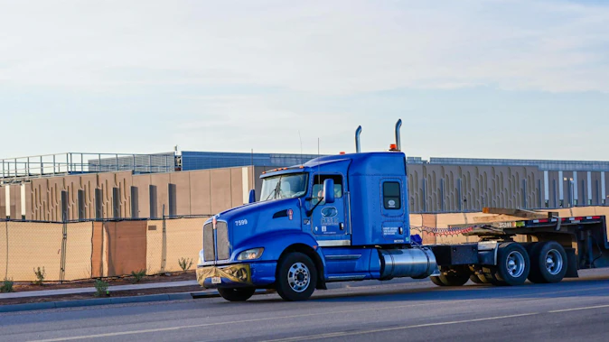 Flatbed semi truck passes a large data center campus under construction