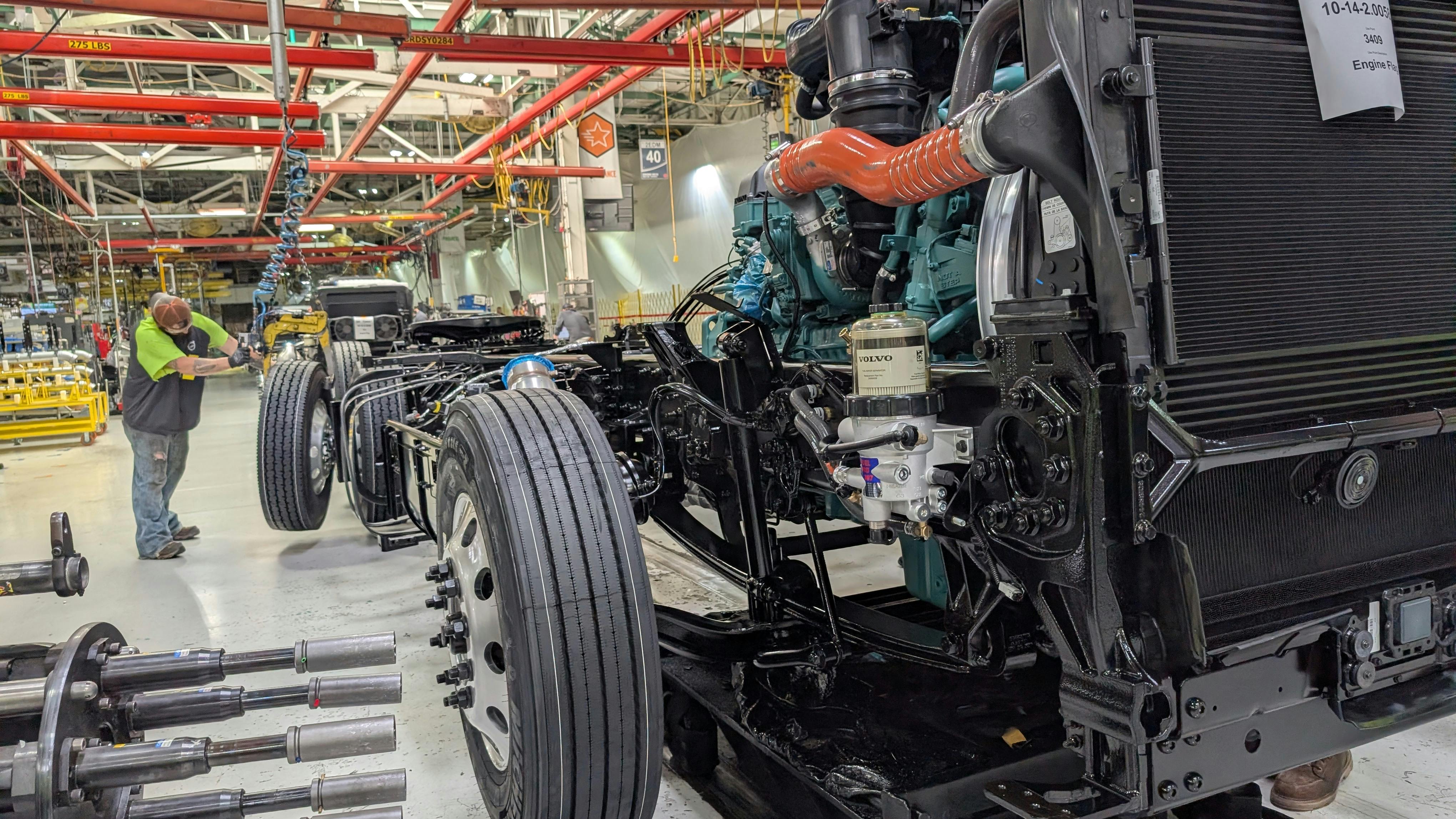 Class 8 semi-truck chassis and diesel engine moving along the assembly line inside a heavy-duty truck manufacturing plant.