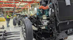 Class 8 semi-truck chassis and diesel engine moving along the assembly line inside a heavy-duty truck manufacturing plant.