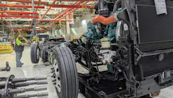 Class 8 semi-truck chassis and diesel engine moving along the assembly line inside a heavy-duty truck manufacturing plant.