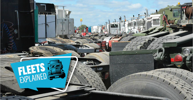 Fleets Explained graphic overlaying a row of preowned commercial semi-trucks parked in a large equipment auction lot.
