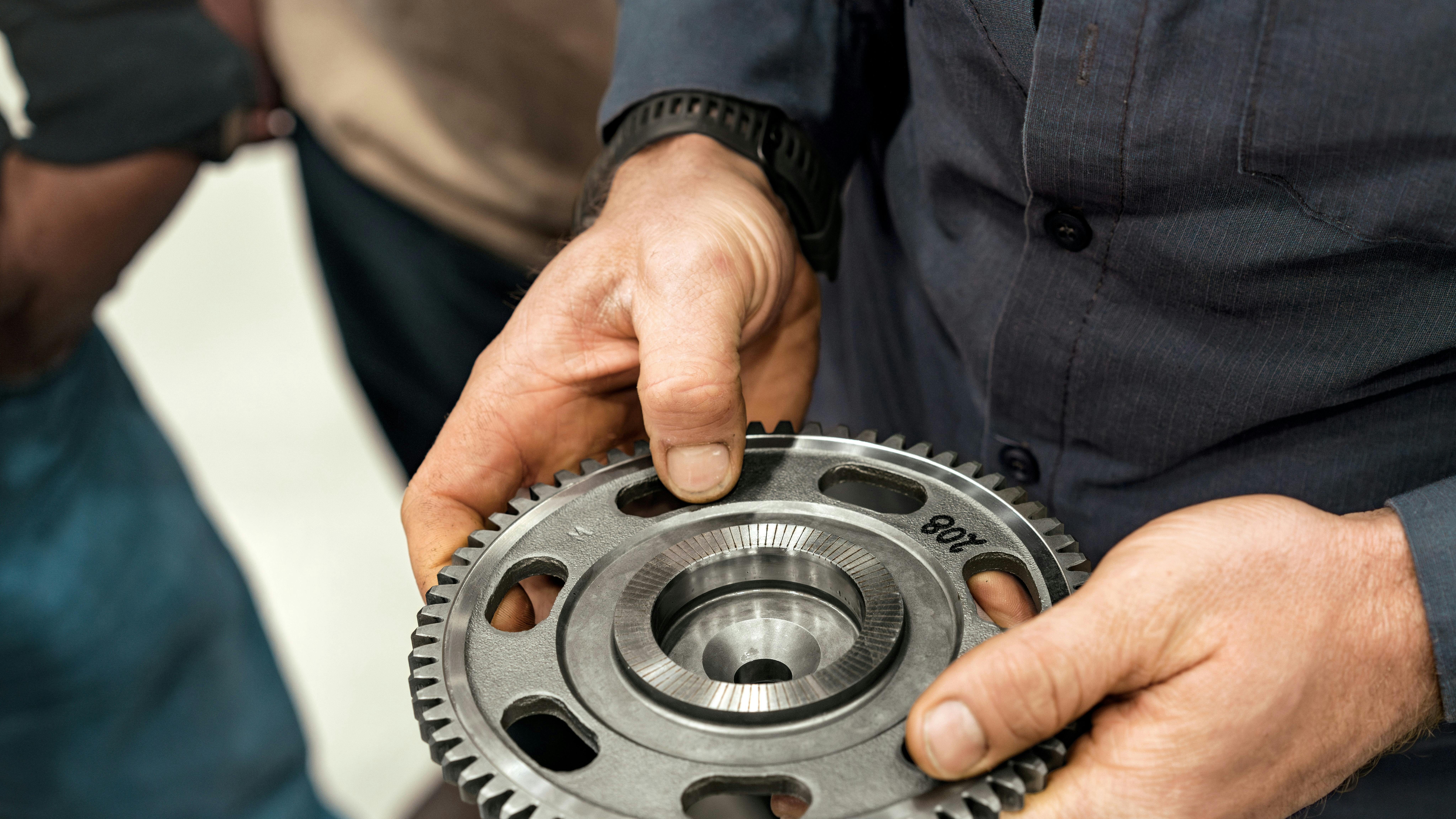 A close-up view of a technician's hands holding and examining a heavy-duty machined metal gear.