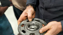 A close-up view of a technician's hands holding and examining a heavy-duty machined metal gear.