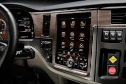 Close-up view of the Peterbilt Paccar Connect digital 13-inch portrait center-stack display featuring a physical 'knob-on-glass' multi-function dial at the bottom, surrounded by woodgrain dashboard trim.
