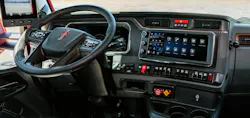 Dashboard view of a Kenworth truck showing the Paccar Connect 15-inch landscape display with its fixed left frame for controls and active apps on the right, above dedicated, tactile physical rotary dials and the Intellipark electronic brake interface.