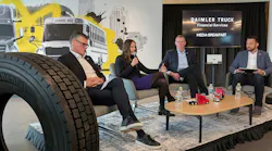 Four Daimler Truck executives sit on a stage during a media briefing in Charlotte in front of a backdrop showing Freightliner trucks and a school bus.