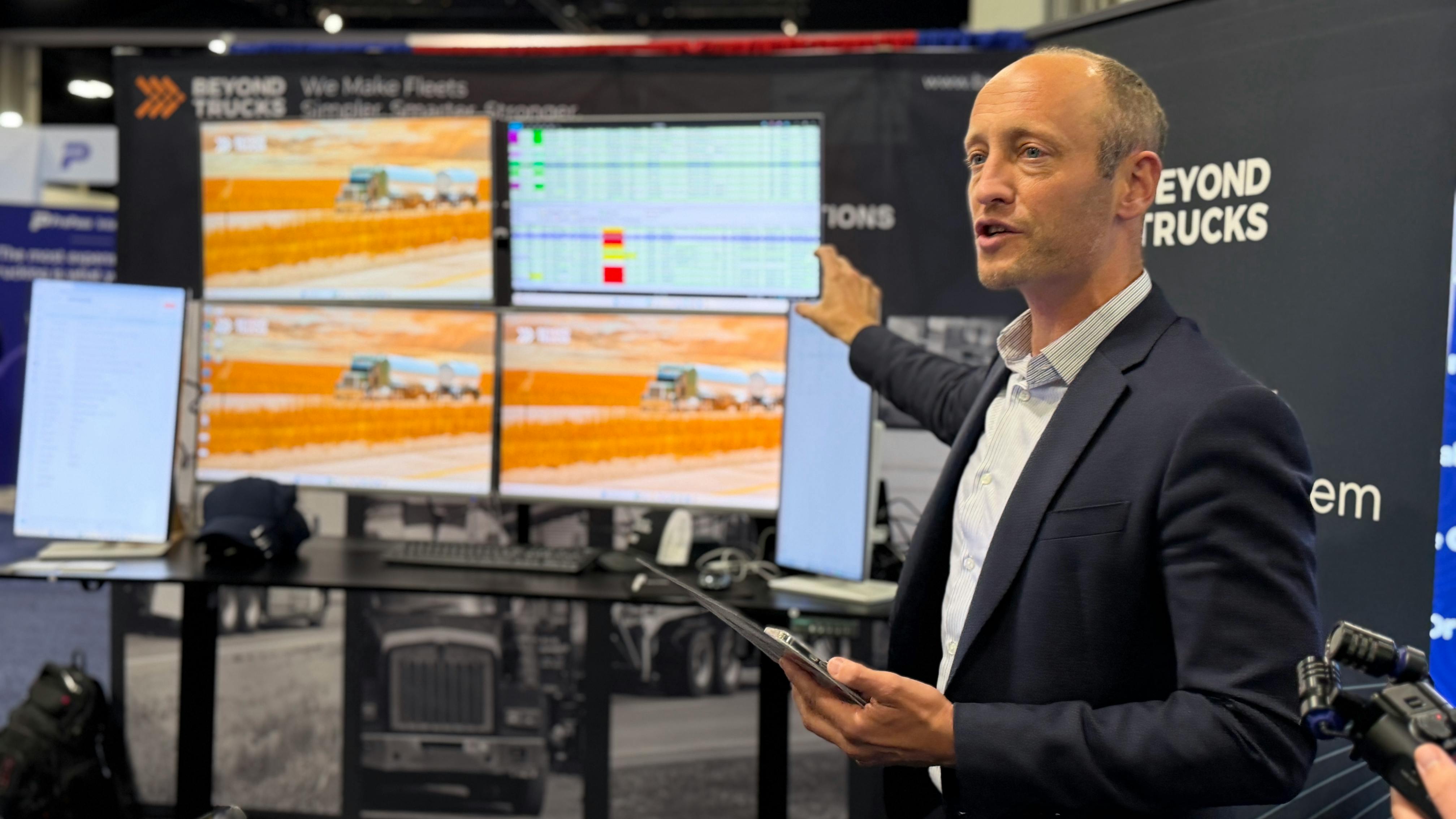 Hans Galland, CEO of BeyondTrucks, gestures toward digital fleet dispatch screens during a product demonstration at ATA MCE.
